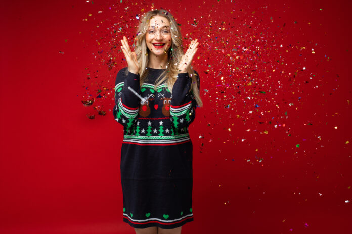 Happy young girl in sparkling confetti celebrating new year and xmas on red studio background