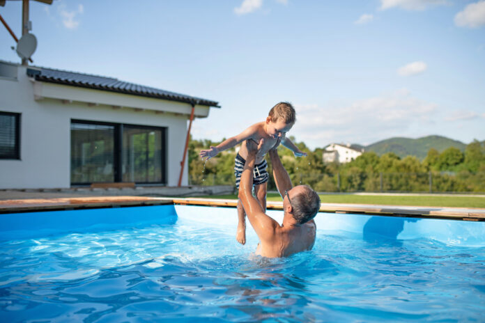 A father with small son playing in swimming pool outdoors.